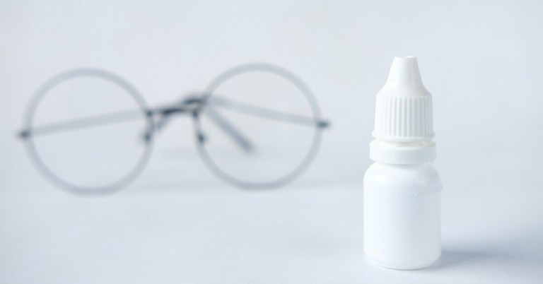Augentropfen-Flasche mit unscharfer Brille im Hintergrund