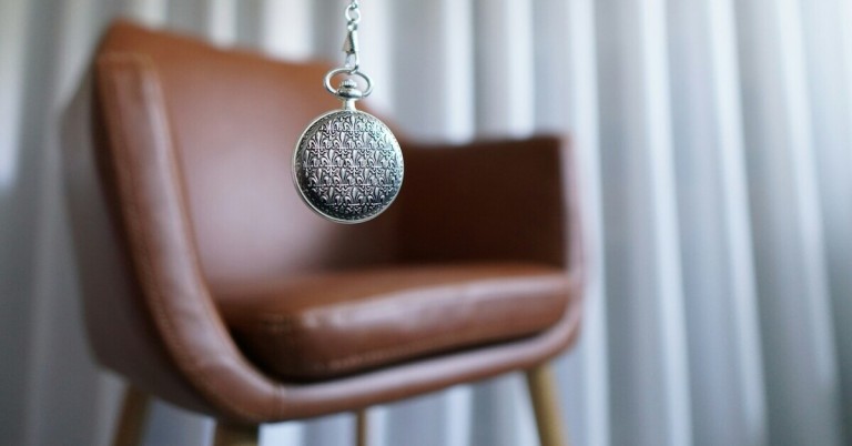 Hypnose mit Taschenuhr vor einem Sessel im Therapieraum