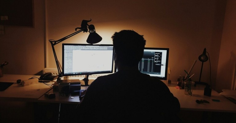Mann sitzt im Dunkeln vor Bildschirm und arbeitet am Computer