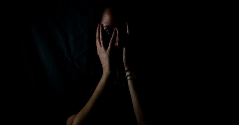 Gesicht im Dunkeln, teilweise verdeckt von Händen, Symbol für Stress