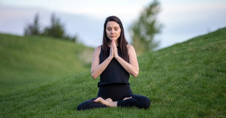 Frau bei Meditation im Gras in entspannter Sitzhaltung