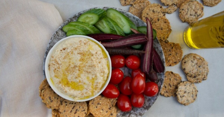Hummus und Gemüse Snack mit Gurken, Karotten, Tomaten und Crackern auf einem Teller