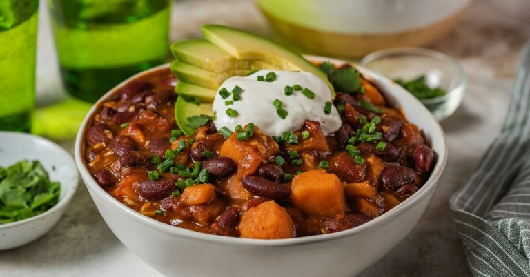Gericht mit Süßkartoffeln und Bohnen, garniert mit Avocado, Sauerrahm und Schnittlauch