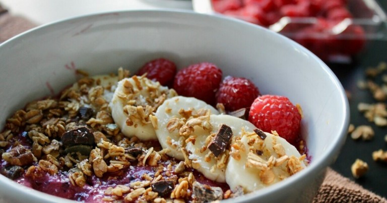 Schale mit Cerealien, Bananenscheiben und Himbeeren als gesundes Frühstück