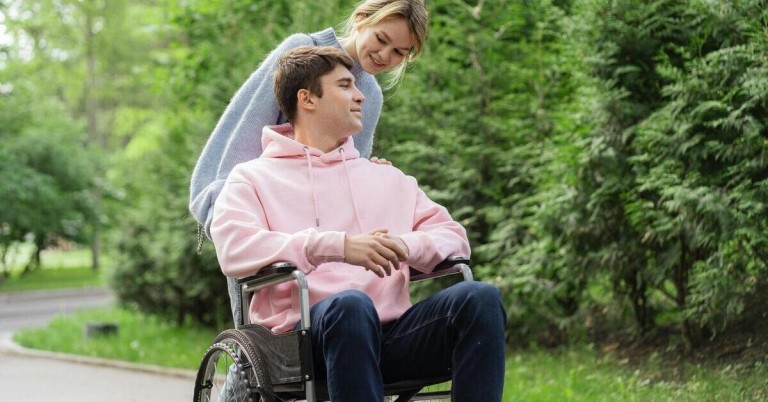 Junger Mann im Rollstuhl wird im Park von einer Frau begleitet