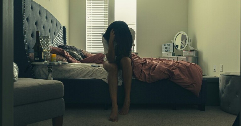 Frau sitzt auf dem Bett und wirkt depressiv in einem abgedunkelten Schlafzimmer