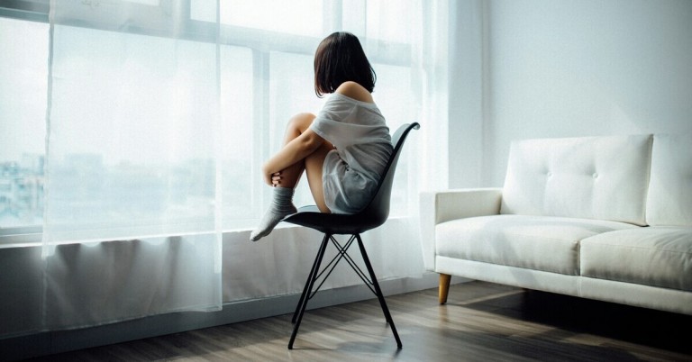 Frau sitzt vor dem Fenster auf einem Stuhl und blickt nach draußen