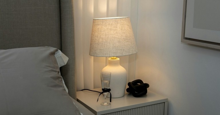 Nachttisch mit Lampe, Glas und Dekoration neben einem Bett