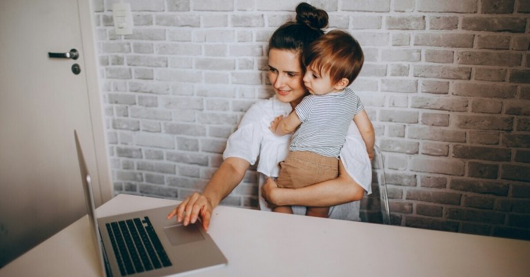 Mama arbeitet am Laptop und hält ihr Kind auf dem Arm