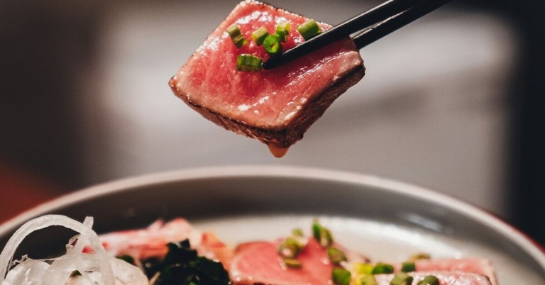 Rohes Rundfleisch in Japan mit Frühlingszwiebeln, Nahaufnahme mit Essstäbchen